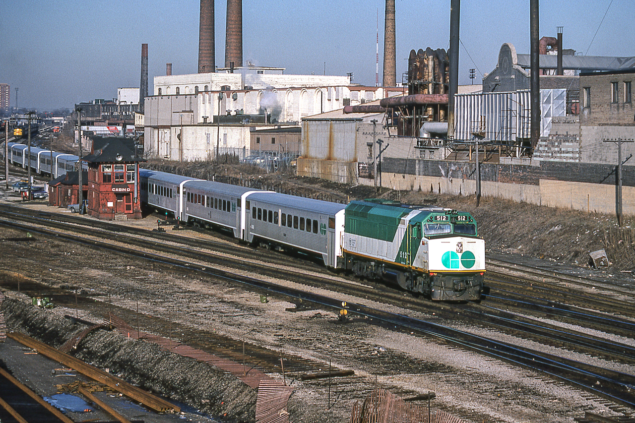 GO 512 and its train head east past Cabin D in Toronto on March 23, 1982. In the far-left background is an eastbound VIA train.