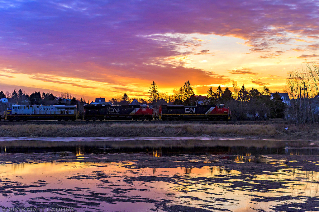 CN 8878 leads stacker train Q120, as they head through Memramcook, New Brunswick, with a colorful sunrise adding a nice backdrop to the shot.