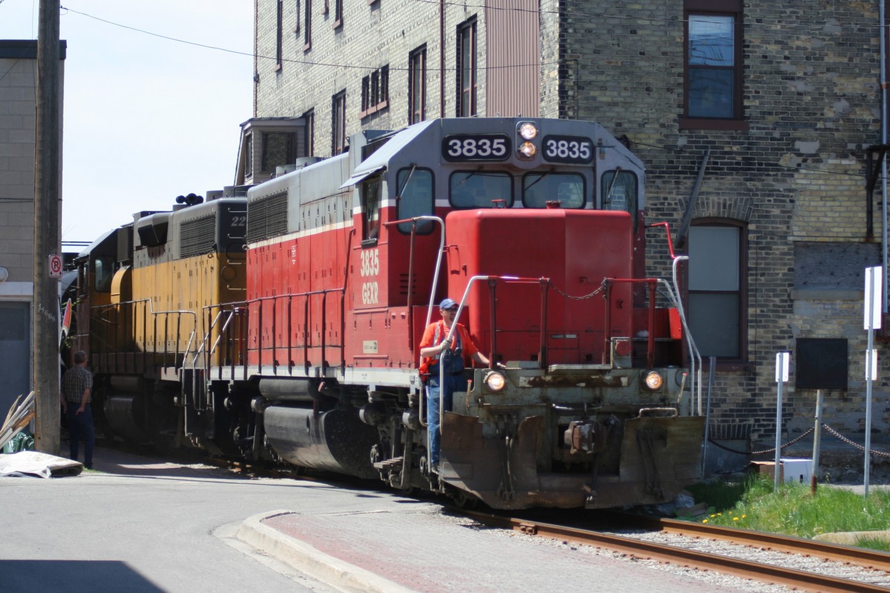 Squeezing through the buildings Goderich-Exeter Railway train X580 is seen approaching Regina Street in uptown Waterloo, Ontario with GEXR GP38AC 3835 and LLPX GP38AC 2210. The train is heading back to Kitchener from Elmira on the Waterloo Spur.