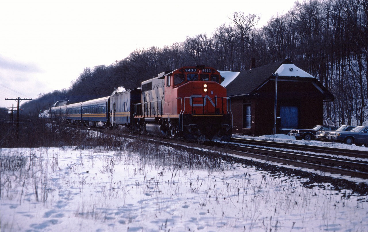 A four-car passenger train pauses a moment at the Dundas station in the winter of 1986. Steam for heating is provided by the steam generator unit and a leased CN GP40-2LW provides the power. In the mid-1980s, VIA leased CN GP40-2LWs and GP40 units to supplement its own aging fleet of 1950s cab units.