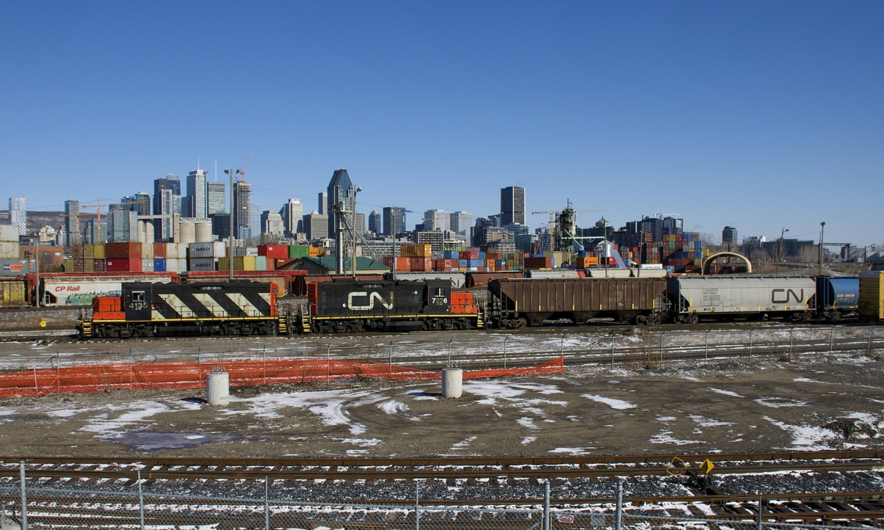 The Pointe St-Charles Switcher with GP9's CN 4135 & CN 7226 is doing some switching in its namesake yard before heading to the East Side Canal Bank Spur with eight grain cars. Behind is the skyline of downtown Montreal.