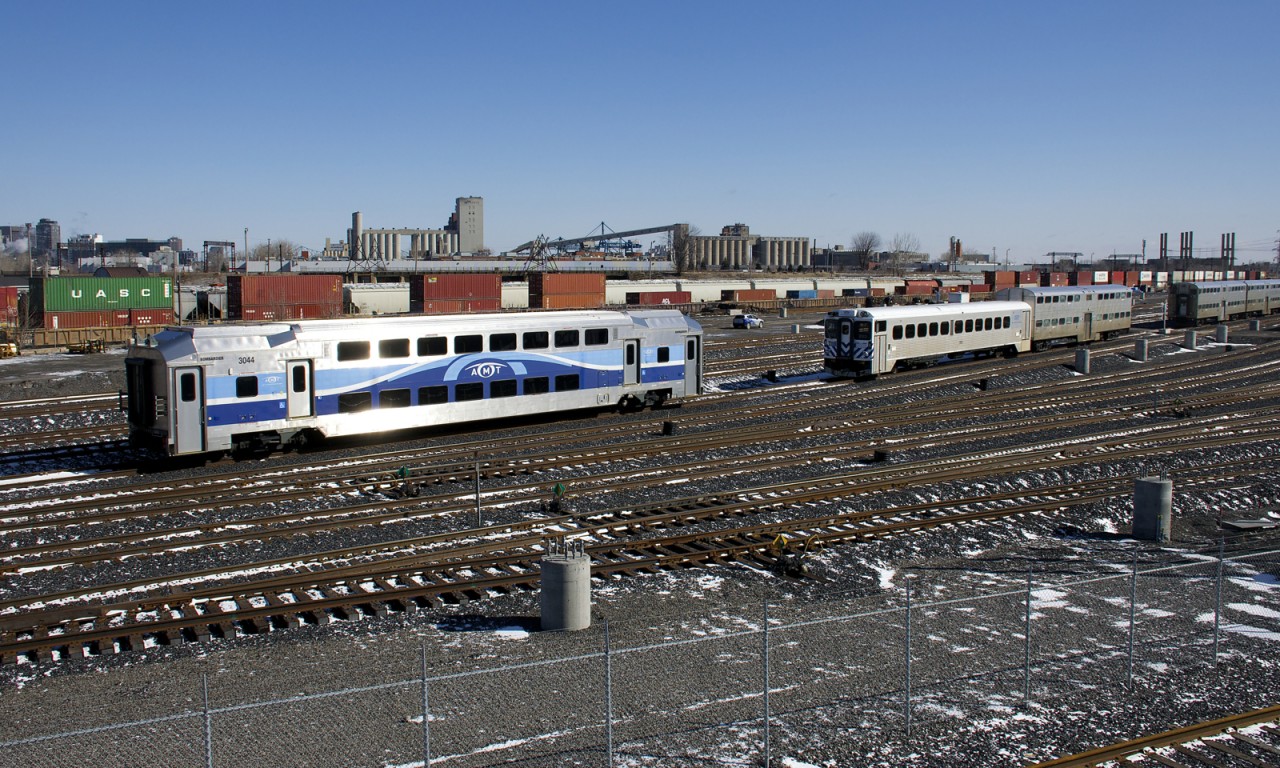 Three generations of commuter cars are visible at the RTM's Pointe St-Charles Maintenance Centre, with multilevel car AMT 3044, single level ex-GO Transit car AMT 203 and a few Vickers gallery cars. In the background CN 120 is passing on CN's Montreal Sub.
