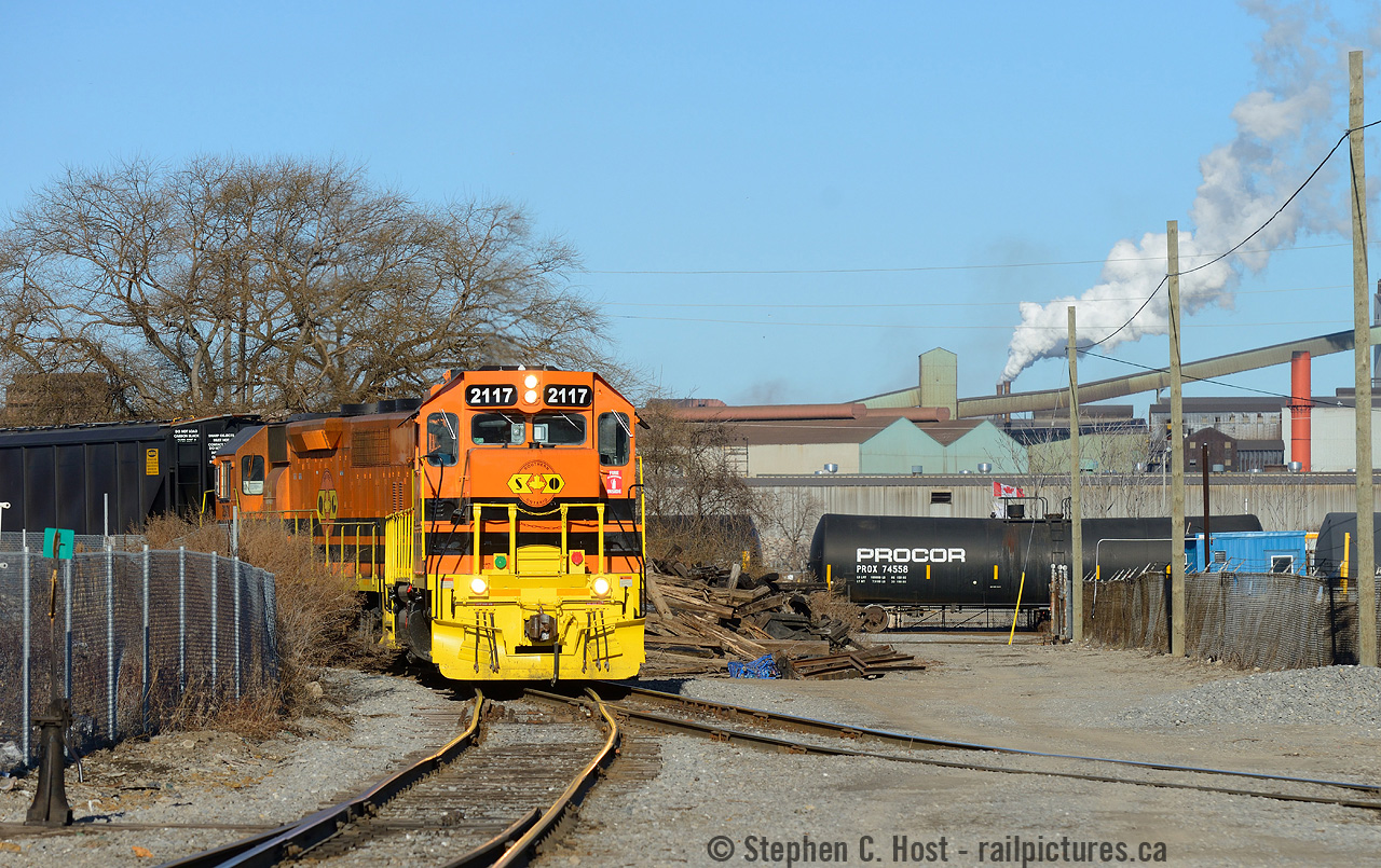 While I usually remark that I spend a lot of time here, one must not remiss the Men and Women who work this line day in and out.. they spend far more time down here then I do, I just tote my big camera every once in a while..
And this is the kind of scene I love to shoot, gritty Hamilton, Dofasco smokestacks, tank cars..  holding tanks for Ruetgers Canada (formerly VFT) at right, and the Orange of G&W looks really really good here. Too bad 2117 has already gone tits up only a month after coming online - let's hope it's rebuilt quickly.