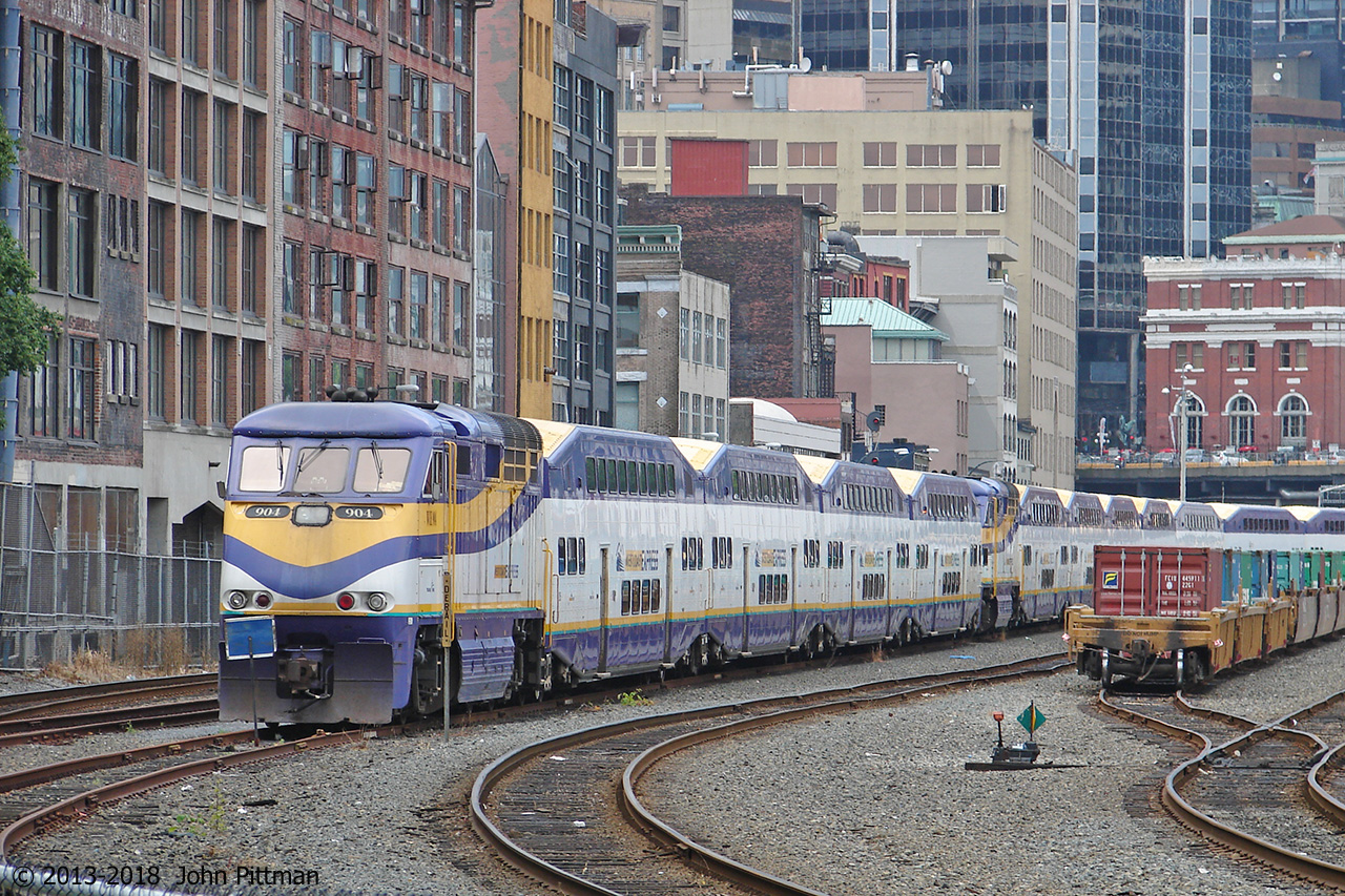 A short West Coast Express train lead by F59phi WCE 904 is tied up in front of a longer train in downtown Vancouver.  Their afternoon/evening assignments will return commuters eastward, ending at Mission BC. 
The red brick building on the right is the West Coast Express / BC Transit Waterfront station, which was built by Canadian Pacific as their Vancouver terminal. 
Yard tracks on the right hold intermodal railcars being staged between the nearby intermodal facilities of the seaport and CP's Port Coquitlam rail yard.