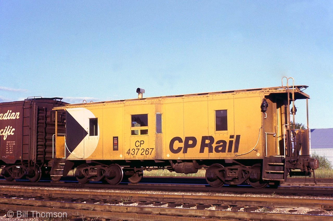 CP Rail bay-window caboose 437267 (or "van" in CP parlance) is pictured sporting the then-modern action yellow livery at Lambton Yard in Toronto. CP built three of these steel bay-window cabooses in 1948 (437265, 437266 & 437267) but the idea never caught on with CP, and further cabooses were built with offset and centre-set cupolas. The three bay-window orphans spent much of their lives in local and transfer service, and 437266 has been preserved in Okotoks AB.

Also notice how short the body is in height, even compared to one of CP's old "minibox" boxcars it's coupled to (an interesting feature is that minibox is one equipped with a small "lumber door" at the A-end, for the old practice of loading/unloading lumber piece-by-piece by hand out the end of the car).