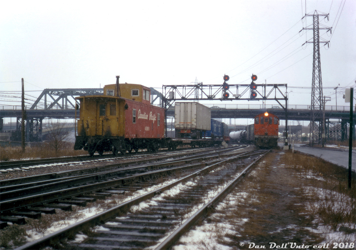 Heading down CP's Don Branch (Belleville Sub) between Leaside to downtown Toronto, CP van (caboose) 438811 brings up the markers on a transfer move from Agincourt to Parkdale/West Toronto, with the "Empress of Agincourt" RSD17 8921 leading the charge solo on the head end. The rear end shown here is ducking under the Queen St. bridge spanning the Don River (entering the "Toronto Terminals Railway Company" trackage as the signalbridge sign denotes), passing CN S2 8136 with a short consist waiting at "Don" on CN's Bala Sub (judging by the CP cars, either lifting or setting off interchange traffic from the Cherry St. freight yards, or switching some of the local industries like S.McCord cement on the right). Some blue CAST containers and piggyback traffic add a nice touch to a gloomy snowy day.  438811 sports the short-lived "action script" livery that CP switched to a year or two before the CP Rail and multimark rebranding of 1968 were introduced. This brief paint scheme was applied to some freight cars (mainly those built new) featuring larger script lettering and number fonts, with various colours applied depending on the use: yellow on insulated boxcars, green on newsprint boxcars (with the pine tree logo), silver on mechanical reefers and pressure-unloading hoppers, and on vans it was red sides with yellow ends. Most of these colour denotations were carried over into the CP Rail era, with vans getting full yellow instead. Original photographer unknown, Kodachrome from the Dan Dell'Unto coll.