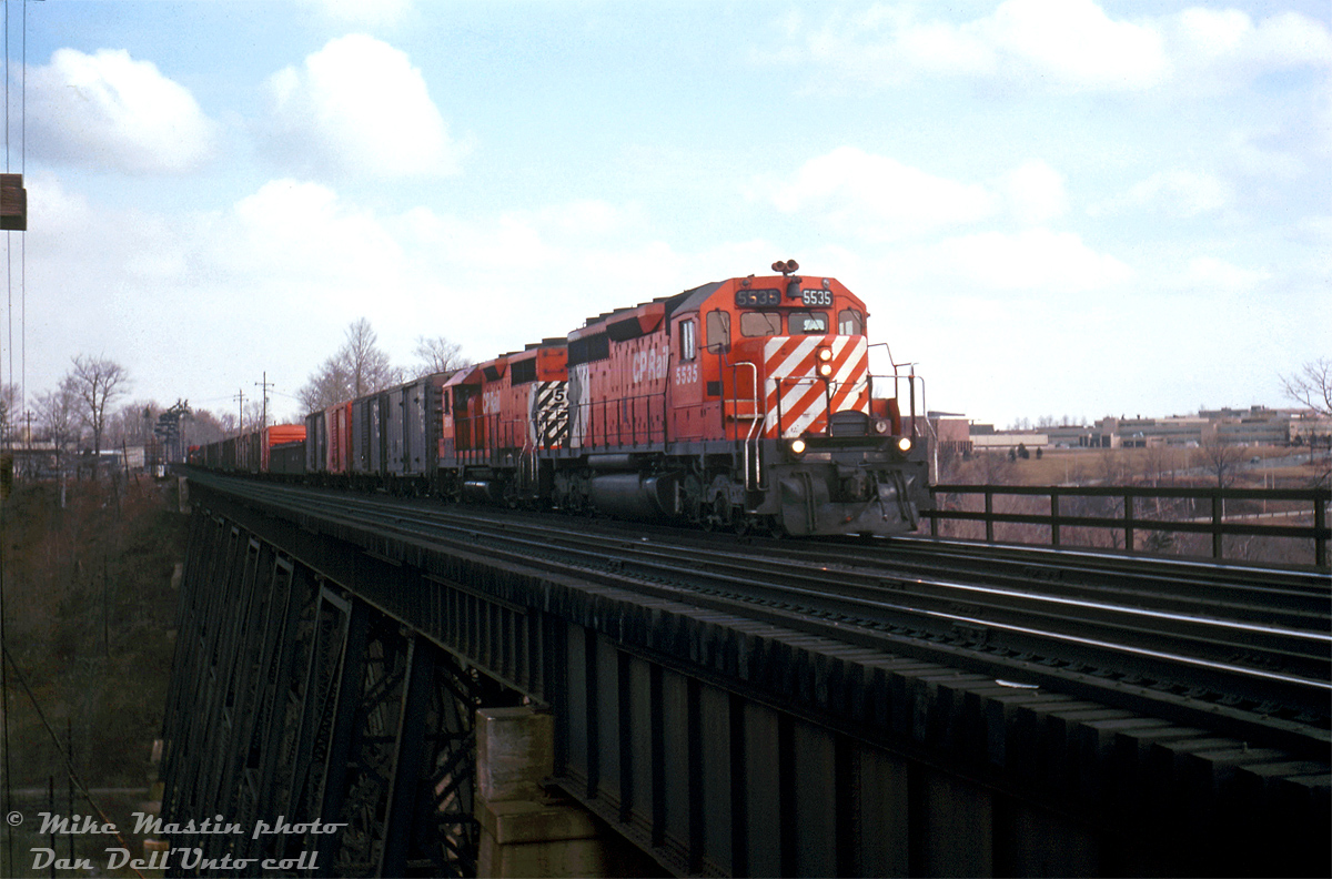 CP SD40 5535 and GP35 5013 head a westbound freight on the Belleville Sub, crossing the high bridge over the West Don River just east of Leaside and west of Donlands (junction with the CN Leaside Spur to Oriole). The trailing 5013 sports a unique version of CP's earlier 5" stripe scheme known as the "Ogden Multi" (with small multimark and stripes only going up 2/3 of the way). A nice cut of 40' boxcars makes up a good portion of the head end.  Visible in the background to the right is IBM's sprawling Don Mills headquarters, at 844 Don Mills Road / 1150 Eglinton Avenue East, which used to have a rail spur coming off the CP's Belleville Sub leading into one of the factory buildings (you can see the large roll-up doors from here).  Mike Mastin photo, colour slide from the Dan Dell'Unto collection.
