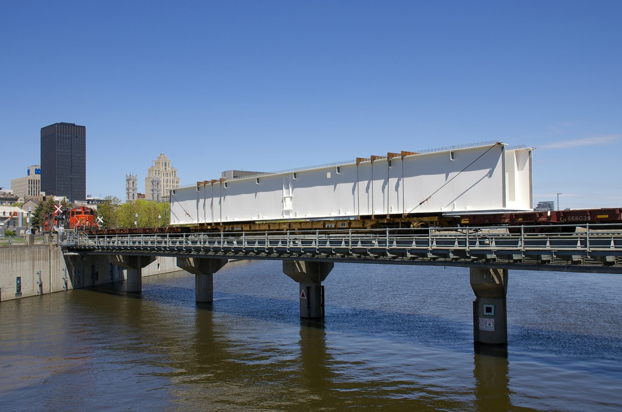 A piece destined for the new Champlain Bridge in Montreal is crossing the bridge over the Lachine Canal, destined for the Port of Montreal, with a second just behind. From there the bridge pieces will reach the work site via barge.