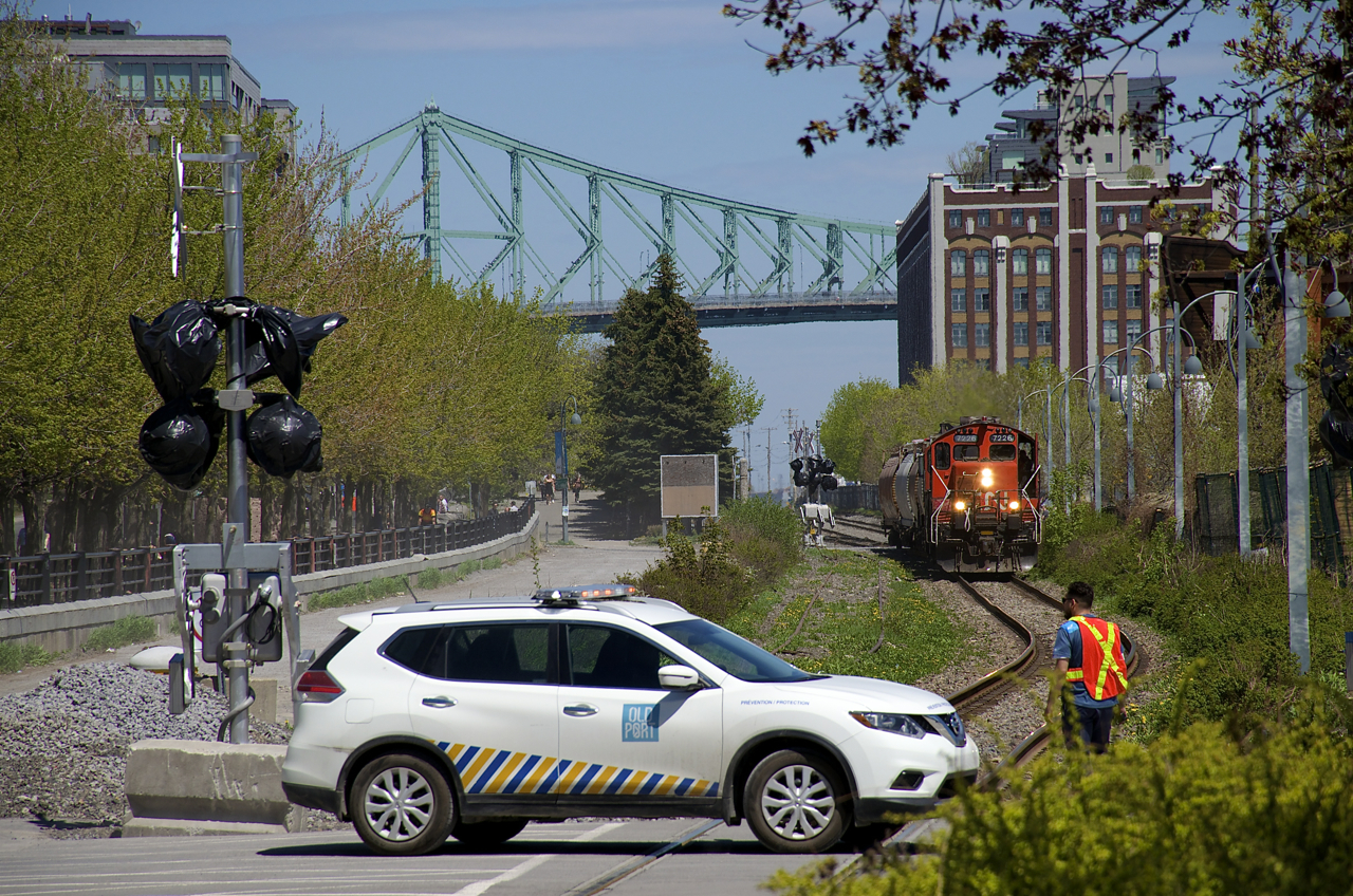 A Port of Montreal truck crosses one of the many crossings in this area, leapfrogging a slowly approaching train so that it can protect another crossing, as a transfer led by CN 7226 approaches. This will soon be rendered unnecessary by crossing gates, seen at left but not yet finished and in use.