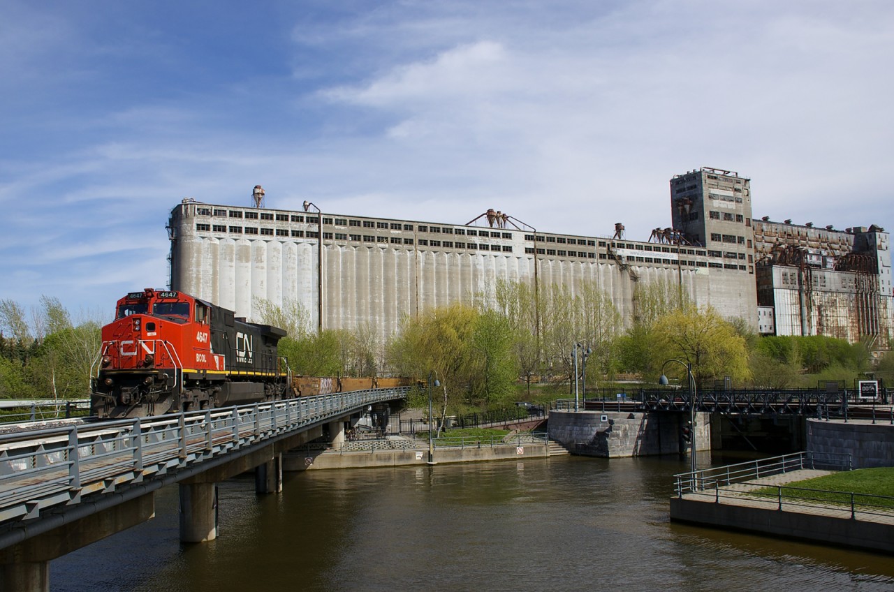 CN 564 with repainted BCOL 4647 as sole power is entering the Port of Montreal with a long string of baretables. Behind the train is the out of use grain elevator #5.