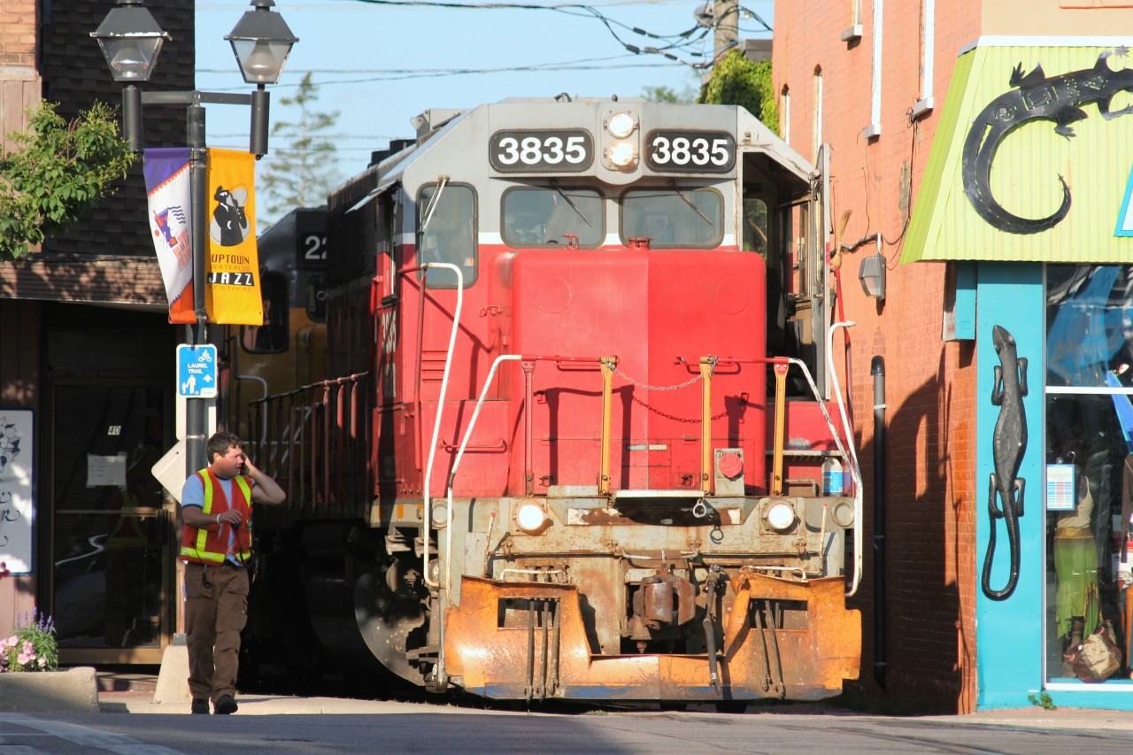 Squeezing through the buildings, Goderich-Exeter Railway (GEXR) train 584 is seen approaching King Street in uptown Waterloo, Ontario with GEXR GP38AC 3835 and LLPX GP38-2 2236. The train is heading north to Elmira from Kitchener on the Waterloo Spur.