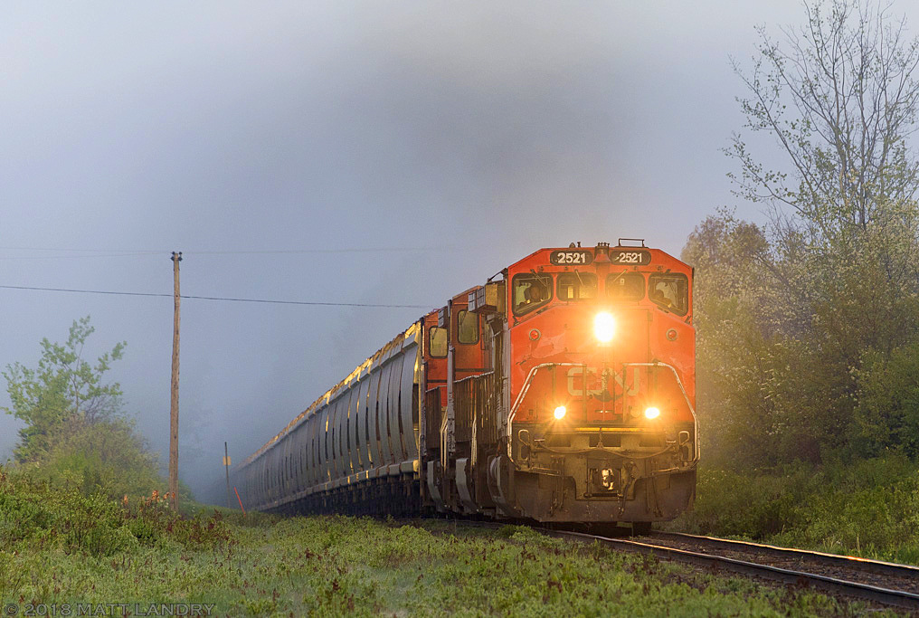 Pulling through the thick fog, CN 2521 leads eastbound potash train L594, as they head up an incline, approaching Apohaqui, New Brunswick, with the early morning sun trying to shine through.