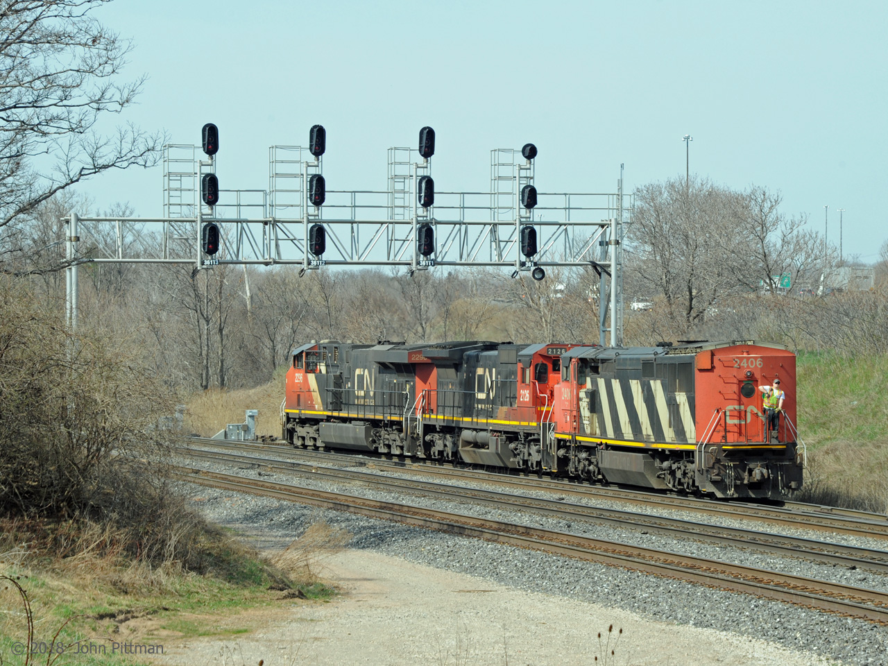 Not seen that often is a cowl body unit leading for several miles tail first, as CN 2406 (C40-8cowl), CN 2126 (C40-8), and CN 2296 (ES44dc) enter the west lead to Aldershot Yard at control point CN Snake. They are front end power of train CN 421, returning after delivering tank cars to RaiLink at Stuart St Yard in Hamilton. The man on the back walkway is guiding the engineer in CN 2296 for this reverse move. 
After completing a lift from Aldershot Yard and rejoining the train, CN 421 will continue to Port Robinson. Midtrain unit CN 2106 (C40-8) will help move the outbound 720 axle train.