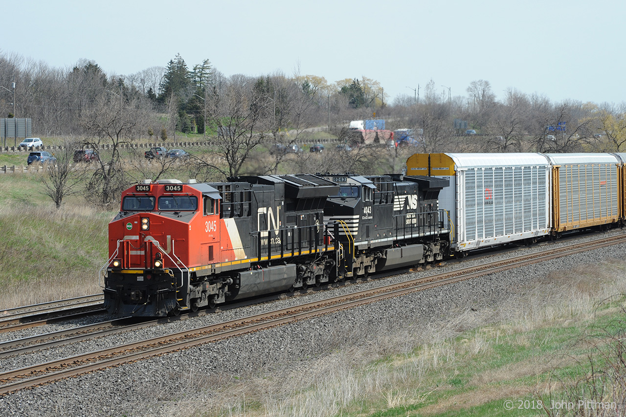 CN 3045 (ET44ac) and NS 4043 (AC44C6M) lead a CN mixed train (397?) downhill west on CN's Oakville Sub.  They are nearing MP 36 and have signals to proceed through CN Snake (Road) and CN Bayview (Junction). 
NS 4043 was remanufactured by NS at Roanoke VA in March 2017 from GE Dash 9-40C unit NS 8805, part of a large program by NS and GE continuing into 2018 and likely to be extended beyond.
Below cabside unit number 4043:  DC to AC \\\ AC44C6M   ( 3-phase AC waveform graphic in the middle )