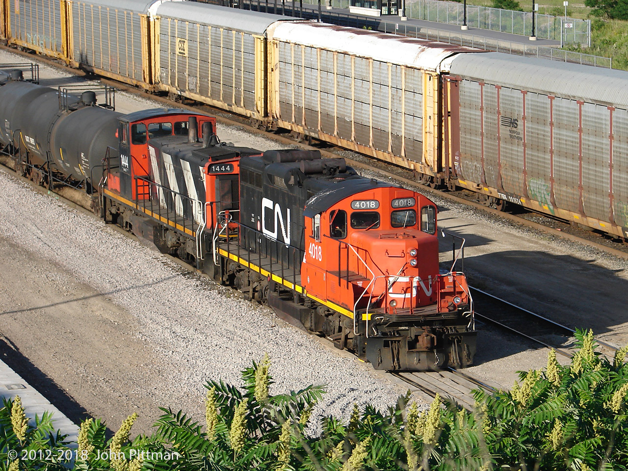 Lighter-weight GP9rm CN 4018 and GMD1 CN 1444 have paused in the afternoon sun with a bouquet of Sumach.  The 4000's are a lot rarer than other CN GP9rm locomotives in my area.  According to Canadian Trackside Guide they are 9000 lb lighter than the other GP9rm's, a 3.5% reduction from the usual 257,000 lb, which could make a difference on lighter rail.  
My photo archive shows that lower number GP9rm's in all series (4000's, 4100's, 7000's, and 7200's) retained the cylindrical CN GP9 exhaust spark arrestors as seen on 4018, but higher number units did not have them.