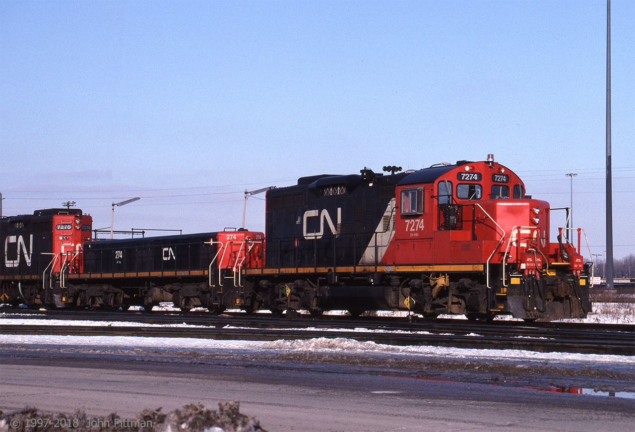 Clean yard switcher CN 7274 (GP9u) in then-new CN colour scheme is well matched with slug CN 274, resting near the Macmillan Yard Diesel Shop. Behind them is similar CN 7270 in the previous mainly black yard engine scheme.  
My reference indicates CN 7274 had previously been CN 4595, before remanufacture by AMF Technotransport in 1993.