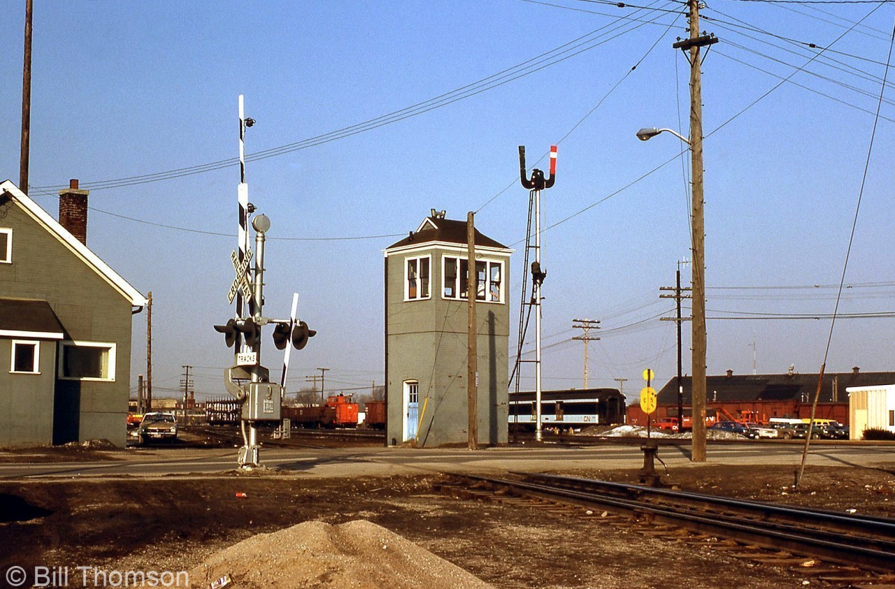 CN "London East" is pictured in March 1977, with the grade crossing tower that stood guard over Egerton Street featured prominently in the middle (new looking gates and crossbucks installed suggest its days are numbered though, and today it's long gone). Note the semaphore signals next to it, and the grey CN paint livery (with blue door) often seen on their lineside buildings and stations. In the background, various old MofW freight cars, orange-painted trucks, and other equipment can be seen in the yard.