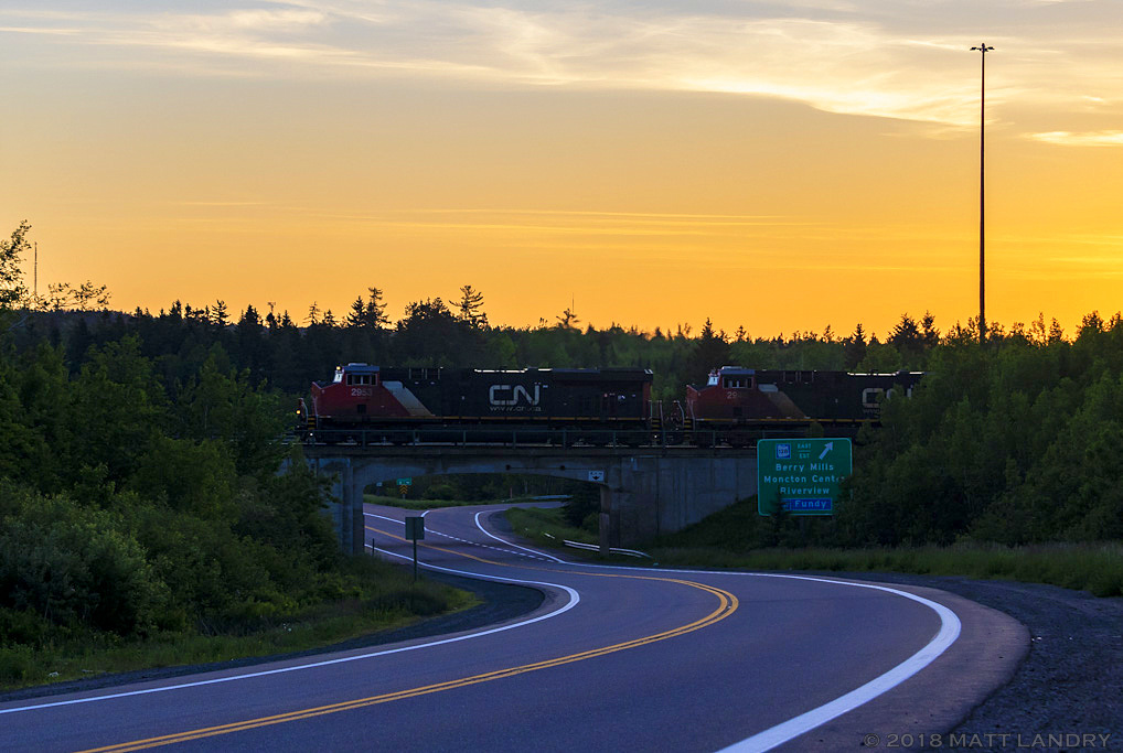 Shortly after departing Moncton at sunrise, CN Q121 rumbles by Berry Mills, New Brunswick, with a nice yellow glow in the sky.