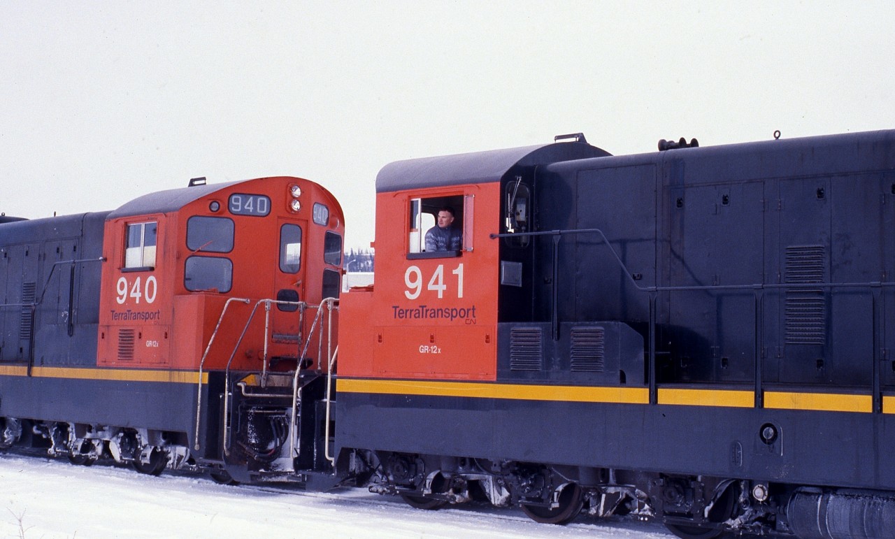 RAILROADER ON THE ROCK. Longtime Engineer Ray Boyd carefully applies the throttle of leading unit NF210 #941 of Terra Transport Mixed Extra 941 West to couple some additional container flats at Grand Falls during Christmas week of 1987. The 1200 horsepower unit with a CN Class of GR-12-x and built by GMD of London Ontario, along with sister 940, was one of 9 in the final order shipped to Newfoundland in 1960. This photo gives an excellent view of the unique end cabs of the NF210's and the very similar NF110's. Its new paint and the excellent maintenance carried out by the shop crews in St. John's belies the fact that these two units were 27 years old. Always well spoken and a consummate gentleman, Ray would later be the 'Mystery Guest' on CBC's 'Front Page Challenge' when the top news story was the shutdown on the Newfoundland Railway!