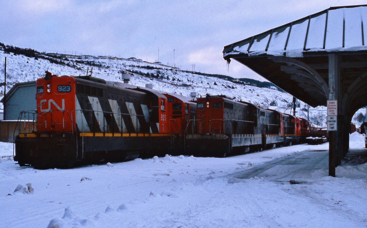 DIESEL DOWNTIME AT DUSK. It's Christmas week 1986 and just before boarding the TerraTransport Roadcruiser Bus to Gambo to visit his girlfriend, the photographer captured this bevy of beautiful NF210's outside the Victorian Era Station in the St. John's Yard. According to former railroader-turned-businessman Peter Byrne, the lights are dimmed on NF210 # 915 so as not to create a glare on the roadway in front of the Newfoundland Railway Shops. The 915 and sister 917 were the only two of the series to wear the small bi-directional TT arrow near the top of the hood, black side cabs and a white skirt stripe when repainted in 1979. Ironically, it was the Roadcruiser that replaced the trans-island passenger train 'Caribou'and spelled the beginning of the end of the narrow gauge railway in 1969. In two years from the time of this photo, 915 would be waiting on the same spot for shipment to the FCAB of Chile while the 923 would be scrapped.