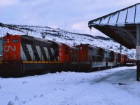 DIESEL DOWNTIME AT DUSK. It's Christmas week 1986 and just before boarding the TerraTransport Roadcruiser Bus to Gambo to visit his girlfriend, the photographer captured this bevy of beautiful NF210's outside the Victorian Era Station in the St. John's Yard. According to former railroader-turned-businessman Peter Byrne, the lights are dimmed on NF210 # 915 so as not to create a glare on the roadway in front of the Newfoundland Railway Shops. The 915 and sister 917 were the only two of the series to wear the small bi-directional TT arrow near the top of the hood, black side cabs and a white skirt stripe when repainted in 1979. Ironically, it was the Roadcruiser that replaced the trans-island passenger train 'Caribou'and spelled the beginning of the end of the narrow gauge railway in 1969. In two years from the time of this photo, 915 would be waiting on the same spot for shipment to the FCAB of Chile while the 923 would be scrapped.