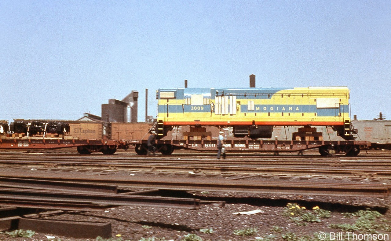 A new GMD London-built EMD G12 for the Mogiana Railroad Company in Brazil (Companhia Mogiana de Estradas de Ferro) numbered 3009 is seen loaded on CN flatcar 663593 at Mimico Yard with trucks on an adjacent flat, being handled by CN enroute for export to Brazil in 1957.

Unit 3009 was part of a 25 unit order of G12's built for Mogiana RR at GMD London between April and July of 1957 (that followed an order of five units, 3001-3005, that were built at EMD La Grange the same year).
