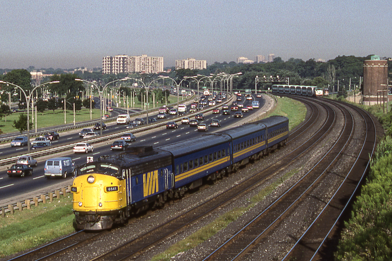 VIA 6541 is eastbound heading towards Toronto Union Station in Toronto on August 9, 1987. Notice both the traffic on the left and the VIA train in the background.