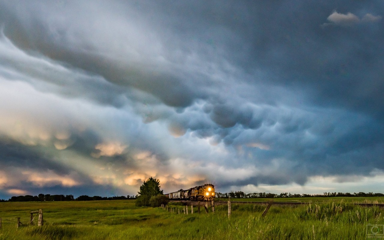 Anticrepuscular rays and mammatus clouds create a dramatic sky as a train comes through the Alberta prairies near Indus, Alberta.