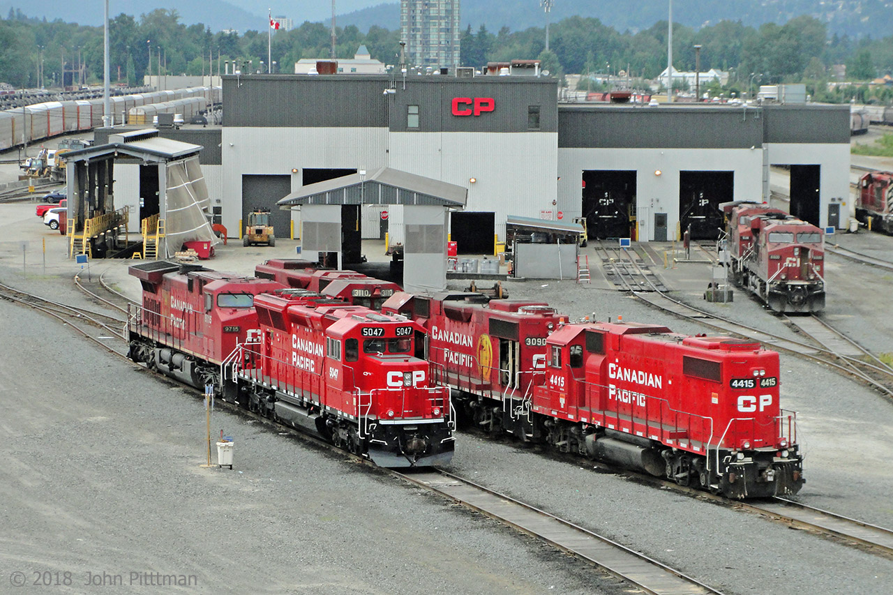 The Coast Meridian Overpass suspension bridge crossing CP's main Vancouver-area yard in Port Coquitlam BC is a good public place to view a large active rail yard and facilities. Some drawbacks for photographers are end-to-end galvanized steel mesh with 46mm square openings, a sidewalk only on the west side, and vibration caused by road traffic. My photos were obtained with a compact camera whose lens fitted through the mesh, though side and down angles were limited.
This north-west facing view shows the Diesel Shop buildings, with a larger than usual percentage of EMD-family locomotives in the area.  The closest row has CP 5047 (SD30C-eco) and CP 9715 (AC4400).  The second row has GP38-2 variants CP 4415 (ex-Soo, no dynamic brakes), CP 3090, and CP 3110. Further to the right are CP 8800 (ES44ac) and CP 9598 (AC4400).