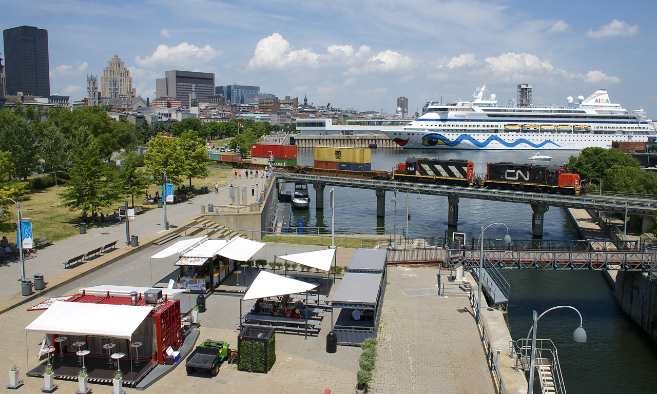 Cruise ship AIDAvita is docked in the Port of Montreal as GP9's CN 7054 & CN 4115 pull some intermodal traffic and baretables destined for track 29 over the Lachine Canal on a sweltering day.
