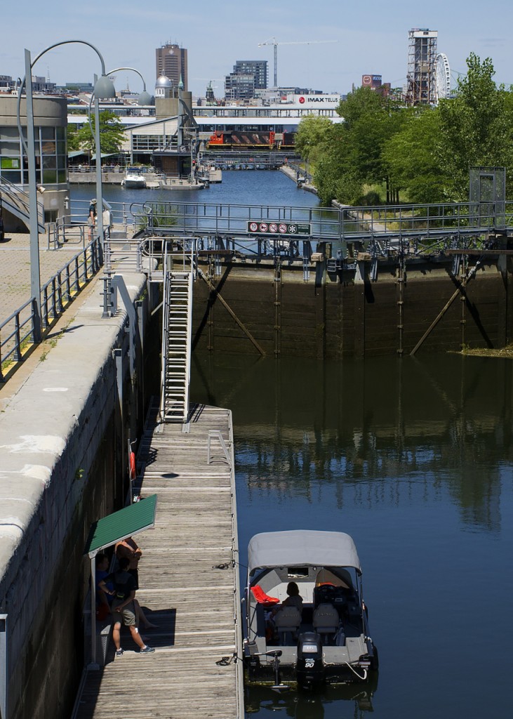 CN 4707 leads a 44-car transfer into the Port of Montreal as it crosses the eastern end of the Lachine Canal, as a boat in the foreground prepares to use one of the locks to continue downstream.