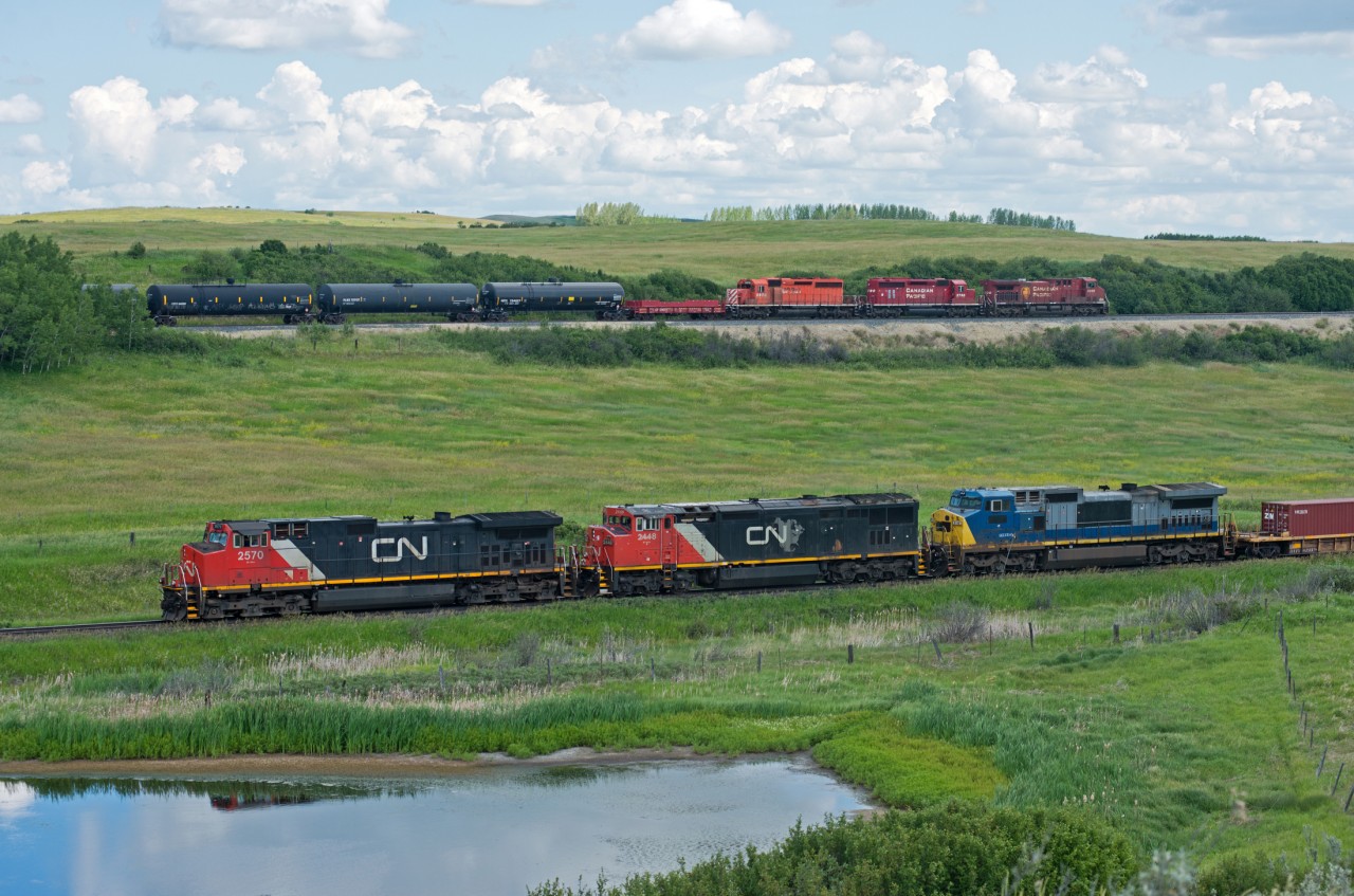 Being in the right place at the right time allowed me to capture this rolling meet between competitors. It was a pretty intense few minutes beforehand as I could hear both trains whistling at nearby crossings. The CP 466 popped into view first with a pleasant surprise in the form of two SD40-2's along for the ride. Seconds later a much slower CN 115 came into view. If this had all happened about ten seconds later, the scene would have been in full sun. That being said I still went away feeling quite satisfied. But there was no time to let it sink in as I made a quick decision to go after the CP. 
 
Now for the numbers's 

CP# 466 (Red Deer-Sutherland) 
CP 8500,5790,5976 

CN# 115 (Toronto-Calgary)
CN 2570,2448,GECX9148