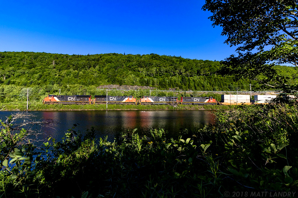 CN stack train Q120 has just crested the uphill climb through Folly Mountain, and are starting their descent, as they rumble through Folly Lake, Nova Scotia, near sunrise.