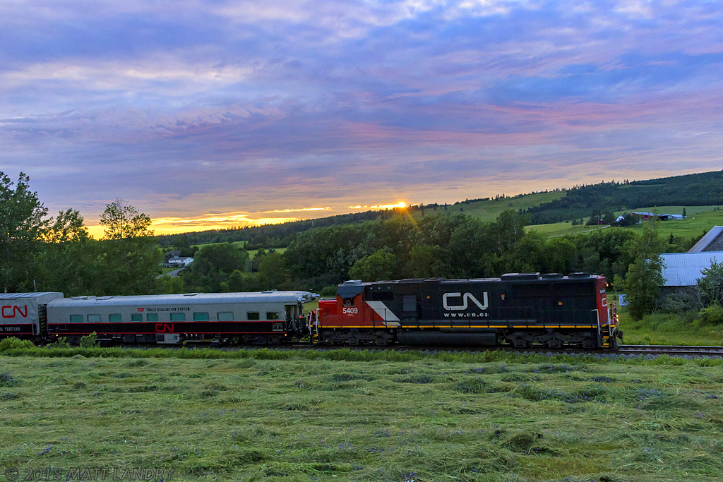 CN 5409, running long hood, leads test train O998, as they rumble by the country side at Norton, New Brunswick, with the sun beginning to set for another day.