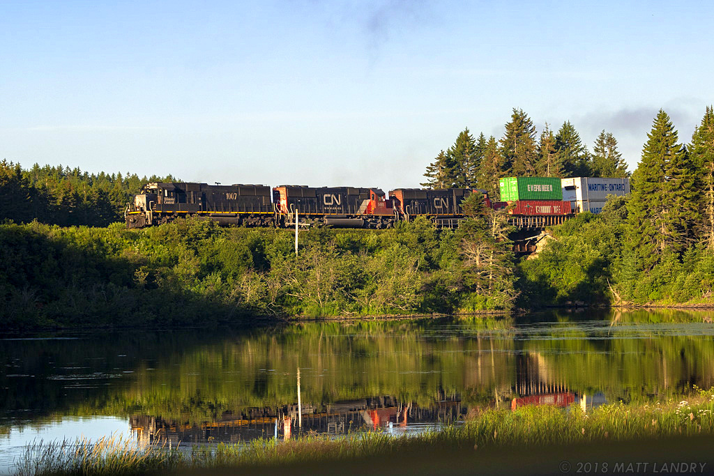 IC 1007 is in charge of eastbound stack train Q120, as they head by Palmers Pond at Dorchester, New Brunswick, near sunrise.