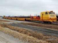 An otherwise overcast and dreary Sunday morning in March yielded a bit of excitement when I came across this elusive 'beast' sitting in the Niagara Falls yard. This multipurpose work unit (including a back hoe/loader that can travel along it's own gondola cars) is Herzog 175, MPM VII. Difficult to photograph due to it's unusual length, it was captured by my camera in three stages. 
Some landmarks visible in the background include the spire of the Saint Patricks church on Victoria Ave, Casino Niagara (ex-Maple Leaf Village) tower, and the Skylon tower.


