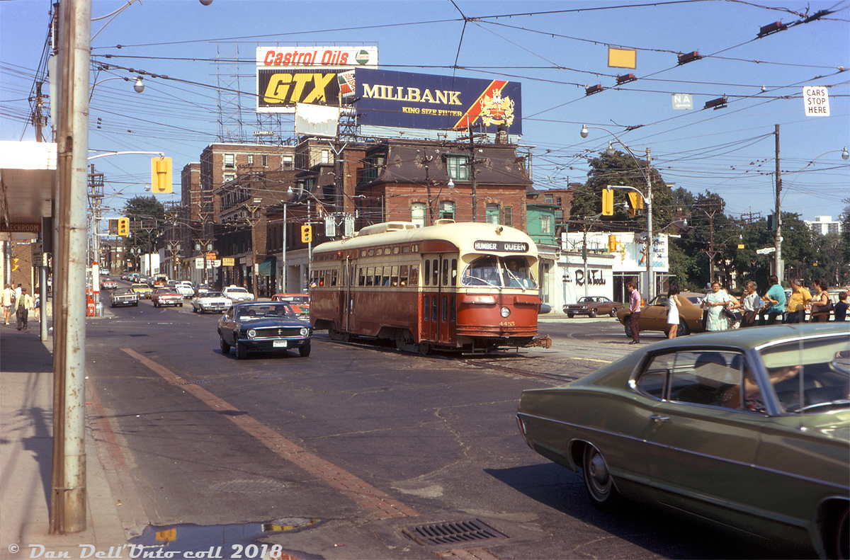 The intersection of Queen Street, King Street, Roncesvalles Avenue and The Queensway in the Sunnyside neighbourhood of Toronto has long been a busy intersection for streetcar traffic, mostly due to the convergance of multiple streetcar routes but also in part due to its proximity to the TTC's Roncesvalles Carhouse a stone's throw away. 

Here on a warm late afternoon summer's day TTC PCC 4455 (an A7-class car bought new in 1947) heads westbound in traffic, rattling across the diamonds and connecting tracks for Roncesvalles-King and crossing from Queen onto The Queenway enroute to Humber Loop. Waiting passengers occupy the stop island in the middle of the road, waiting for the next eastbound Queen car to arrive. The photographer is standing on the sidewalk next to the old Gray Coach Lines Sunnyside bus terminal, and the usual assortment of late 60's/early 70's automotive iron is present (including that rather nice dark blue Mustang). Air conditioning may have been an optional extra in cars of that era, but for most TTC transit vehicles back then (including their fleet of PCC streetcars) the de-facto method of A/C was still propping the window next to you open and enjoying the breeze with your elbow sticking out.

Original photographer unknown (possibly a Dennis Cowley slide), Dan Dell'Unto collection with some colour correction/touch-ups.