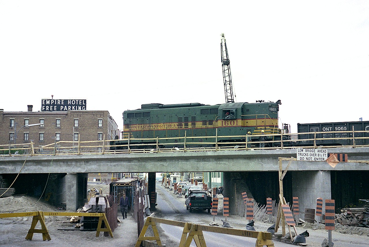 Lots of heavy work going on in the summer of 1977 on the main road into Timmins. Algonquin Blvd (E) or, if you prefer, Hwy 101 is undergoing an increased road clearance where the ONR line into town crosses over and to the station and shop/turntable a couple of blocks south. Apparently the good news would be that even if it is hot and dusty work, the local watering hole is not far away.  ONR 1601 with a work train moves slowly into town. Last I heard this old GP was still around. The line into Timmins was pulled up in the mid 1980s.