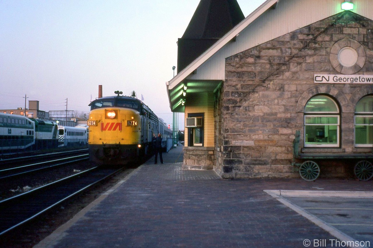 Evening has fallen, and VIA FPA4 6774 on detouring train 79 is seen passing by the old VIA/CN Georgetown Station getting hooped up its train orders from the operator. VIA 79 is detouring off its normal Oakville Sub/Dundas Sub routing this evening due to a wreck at Paris on CN's Dundas Sub. Note the old baggage cart tucked away at the side of the station, and two GO Transit consists parked on the same track (one with an F40PH and the other a single-level cab car) in the Georgetown commuter yard.