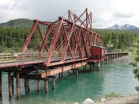 The most impressive bridge on the Canadian side of the White Pass & Yukon Route seems to be this one, crossing the narrows between Bennett Lake and Nares Lake at Carcross Yukon. Carcross is a contraction of caribou crossing, which presumably was a common occurrence here when the town was named.<br><br>
It appears that this bridge was built as a swing bridge, so that it would not impede the riverboat traffic on this waterway. Riverboat transportation has ended, and there are fixed bridges either side of this one - for the Yukon Highway and a footbridge. So it made sense to strengthen this railway bridge from below with additional steel and supports, rendering it immovable. Note also the conduit pipes and wires that crossing the bridge. <br><br>
Carcross WP&YR station is a short distance behind this viewpoint, with the end of in-service track probably less than a mile past that. The active track can be seen curving to the right, as the line follows the east shore of Lake Bennett southward toward Bennett, Fraser, and Skagway.