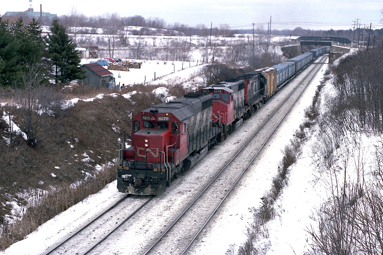 A couple of things are interesting about this image. For those familiar with the bridge over the tracks by Mile 1, Dundas Sub; the nearby Academy can be seen in the extreme upper left.  The old Guelph Rd overpass, which had been propped up for better clearance a long time ago is no longer, having been replaced some years ago. The absence of the foliage seen these days is remarkable.  And this is the 'CAST' train. I remember it on CN, I remember it on CP, but what I don't remember is what happened to it all.  Anyone??
Power on this westbound is CN 5075, 9478 and 3224. An SD-40, GP40-2 and an MLW C-424. Interesting combination.