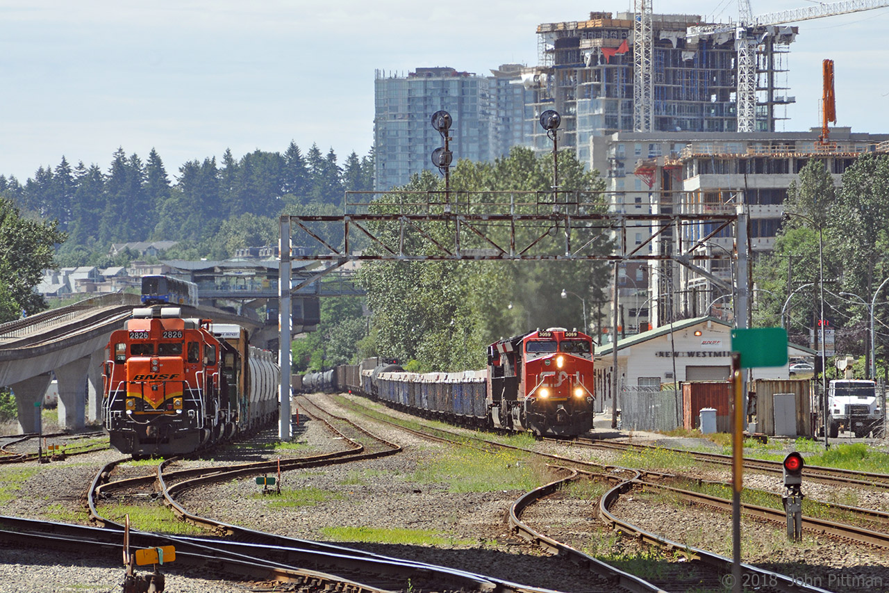 One train approaching, one at rest, one receding.
The approaching CN freight lead by CN 3059 and CN 3060 is heading north-east past BNSF's New Westminster freight station on one of the 2 hot tracks, while BNSF GP39m 2826 (EMD turbo 12-645 and AR10 generator in GP30 body) rests in a siding ahead of BNSF 3149 (GP25), BNSF 2112 (GP38 in BN green), and their train. A Millenium Line Skytrain is heading away toward Sapperton station.
The CN train probably crossed the Fraser River on the CN/BNSF New Westminster swing bridge from Port Mann-Surrey minutes earlier. It will continue on the New Westminster sub, following the track north-west at the wye just east of my vantage point at Braid Street grade crossing. Based on its railcars, my guess is that the CN train will branch off for North Vancouver through the Thornton Tunnel and over the Second Narrows rail bridge. (Vancouver downtown yards and south Burrard Inlet port mostly handle intermodal containers and grain.)