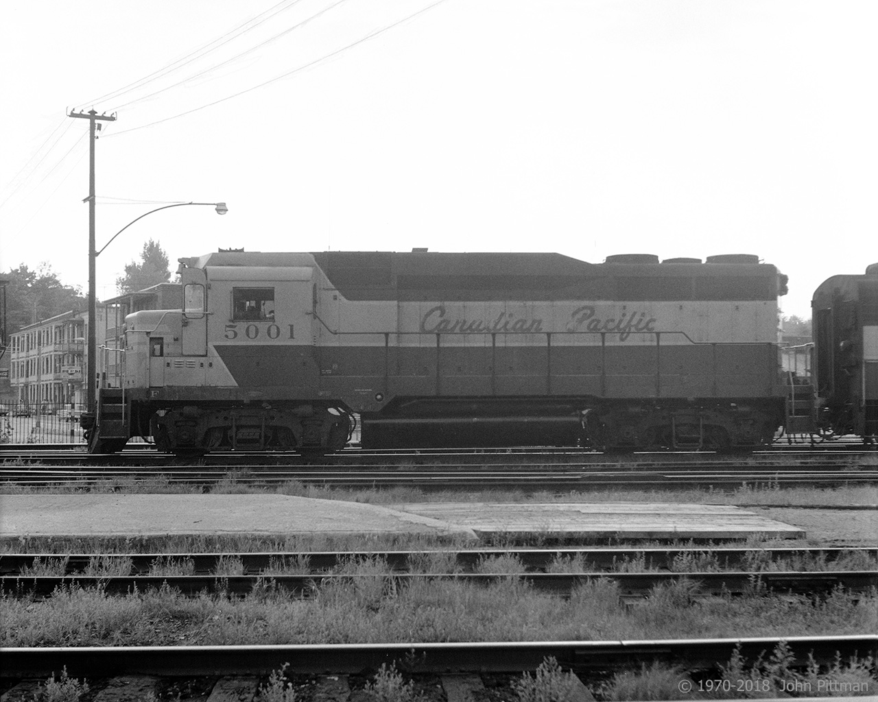 CP 5001, one of 2 GP30's sold in Canada, is just starting the afternoon freight moving at Trois-Rivieres, returning to Montreal with quite a number of newsprint boxcars loaded at the local paper mills and other freight. The trailing unit on this occasion is an FA-2.
In 1970 I saw predominantly 4-axle MLW units on the afternoon freight returning to Montreal from Trois-Rivieres. Three units was typical, otherwise 2 or 4; they would include mixtures of RS11, RS10, RS3, FA, FB, and C424. Other than the occasional freight FP7A, the first GM unit I encountered was the GP35 - I heard its turbo-supercharger whine as I bicycled along the road beside the roundhouse, and wondered what I was about to see.
This GP30 was obviously related but styled differently from the GP35, while its CP class id plate DRF-22a showed lower horsepower than GP35's DRF-25a (or b,c,d).
At the time I valued direct side views of locomotives far above any other angle. The only place that worked well for that in T-R was the station side of the tracks. Unfortunately that put me on the east side, not so good when the sun is going down to the west - most of my best afternoon shots from this era were taken when overcast.
This image of CP 5001, taken toward the setting sun, was very difficult to make a satisfactory black and white print from - only because of its rarity did I save the negative. Fortunately photoshop is easier than darkroom burning, dodging and developing with chemicals. 
48 years separate my first GP30 and latest (BNSF GP39M) images; I hope to catch some more.