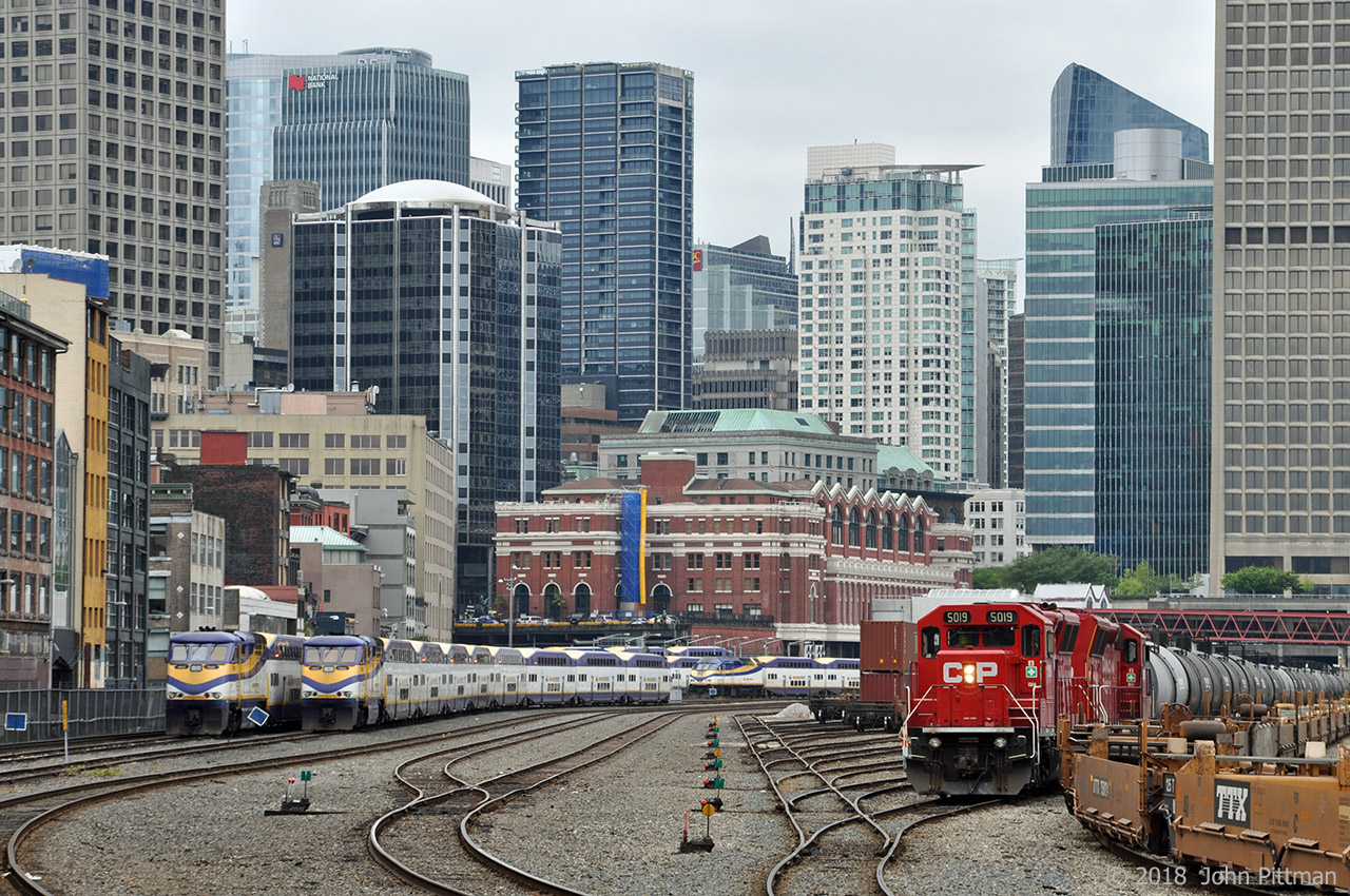 West Coast Express trains are in their usual daytime layover places, east of the red brick ex-CP Waterfront Station (also a terminus for Skytrains and Seabus from North Van).  On the left (south) side is the back of Vancouver's Gastown tourist area (steam clock, etc).  The closer WCE locomotives are 2 of the 5 original F59PHi - WCE 901 and WCE 903.  Closer to the station is WCE 906, the one Motive Power Industries MP36PH-3C that WCE operates - recognizable by its single number board and dark blue paint (instead of purple).  As of 2018 WCE has 6 locomotives available to push 5 inbound and pull 5 outbound rush hour trains from/to Mission BC, leaving one free to receive maintenance. 
CP 5019 and CP 5005 are pumping up the air on a train of tank cars that will be transferred eastward (at least to start); this yard has been CP's western end of track in downtown Vancouver for some years.  Most of the railcars found in this yard are intermodal well cars staging here en route between the nearby Vancouver Container port and Port Coquitlam Yard. 
For the most part, this rail corridor between Vancouver downtown and several miles to the east is secured by 8 foot high chain link fence with 3 strands of barbed wire on top.  This image was taken from the public side of the fence.