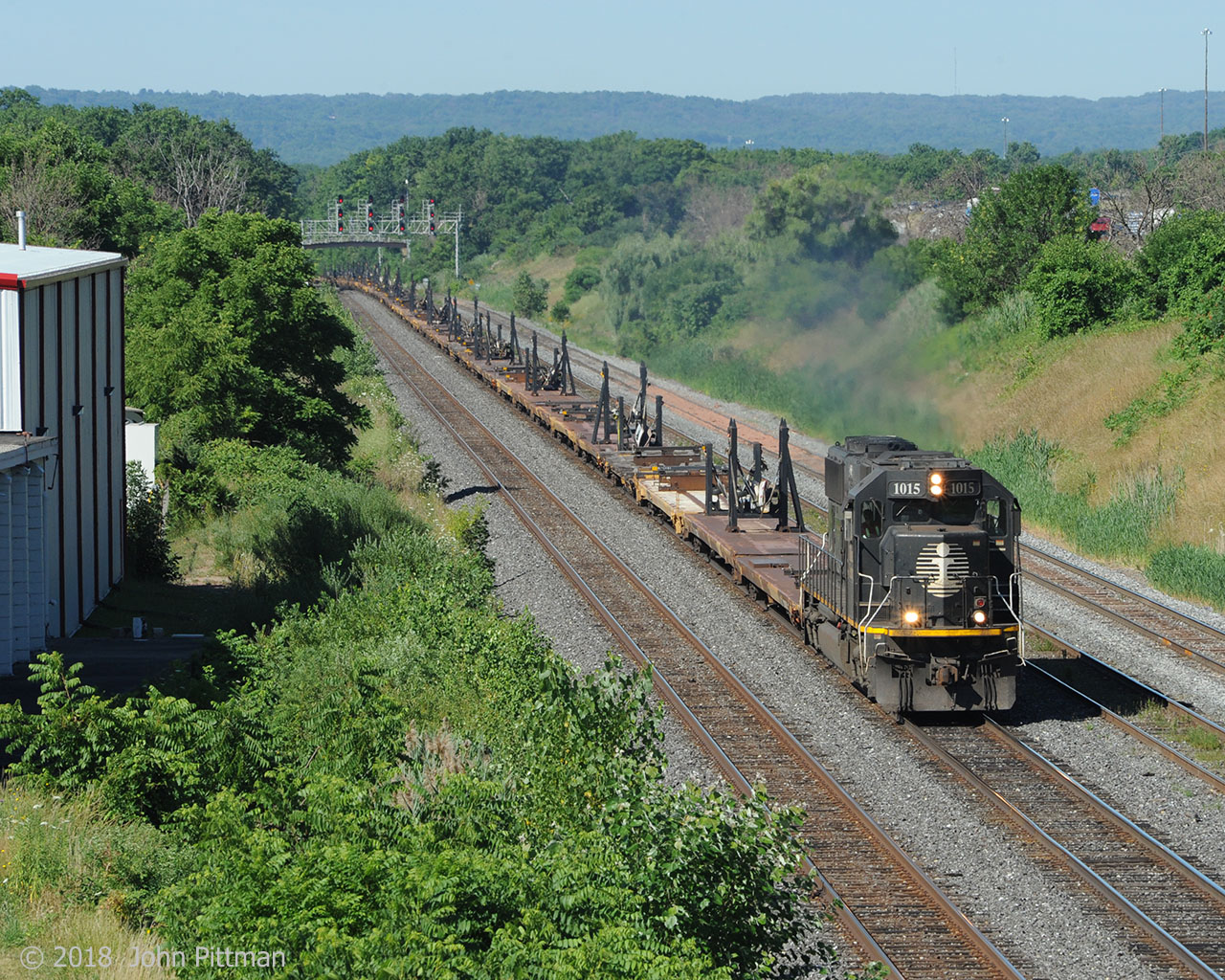 IC 1015 pulls 72 empty flatcars with windmill blade carriers upgrade east on the Oakville Sub. The westbound signals for CN Snake (Road) are in the distance. 
The industrial building on the left seems to have been built here for railway access; it still has a rail-side platform and loading doors, but its siding track was removed in the previous century.