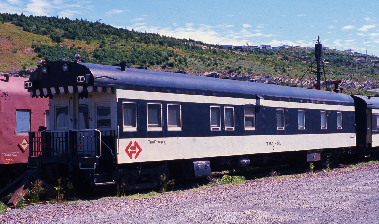 BUSINESS CAR BASKING. TerraTransport's Business Car 'Terra Nova 2' is seen basking in the hot sun of August 7, 1988. Originally built in May 1955 as the 8-Section, 1 State Room, 1 Smoking Room sleeper # 317 'Bonavista' by the CC&F, it was the last narrow gauge sleeping car ordered for the CNR's Newfoundland operations. A vital part of the 'Caribou's' consist, and delivered in all olive green livery, it would be repainted later in olive, black and gold and again in the black and grey before the end of passenger service in 1969. With the formation of TerraTransport in 1979, it was converted to a business car at a cost in excess of $250,000, complete with mahogany walls, a new observation platform and marker lights. While technically still on active duty at the time of this photo, with 7 weeks before the shutdown, it would never again ride the rails in revenue service. Having been sold and resold several times, including as a main attraction at the Trinity Loop Train Park where it could be rented for the night, it eventually found its way to the Orangedale Railway Station Museum in Nova Scotia where it remains to this day.