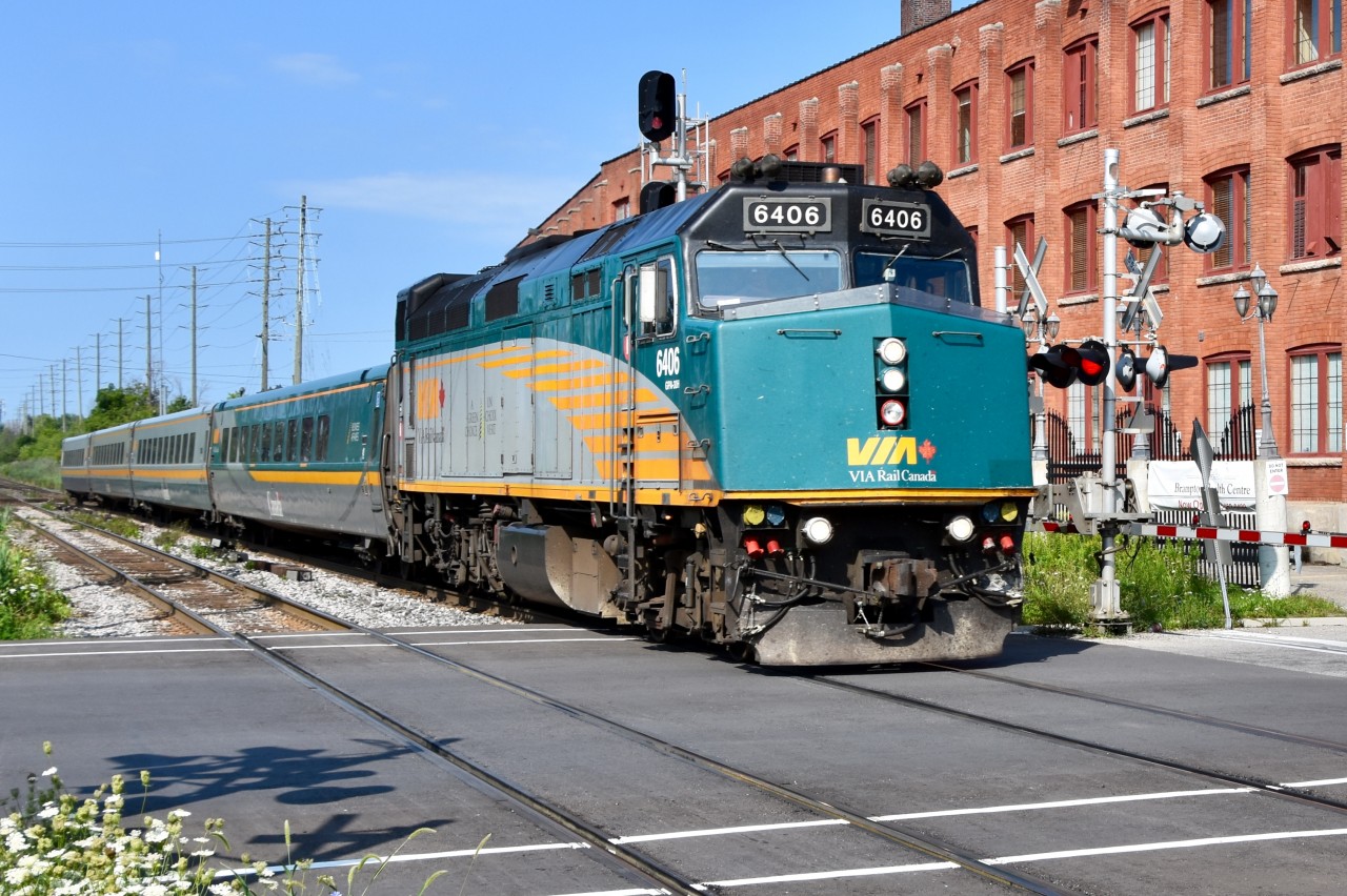 VIA train 84 is arriving at the Downtown Brampton GO/VIA on time to let a few people on. They are crossing over the Mill st crossing which has been repaved just this past July actually with F40-PH 6406 leading.   The building on the right hand side known as The Old Shoe Factory plays a role in the history of the rail lines here actually. Notice how the building begins to curve to the south just after the signal post. This is because the old CN/CP interchange track ran right alongside the building back in the day when CP ran to Owensound. Most of the rails for the old CN/CP interchange track are still in place rotting away but if the GO trains ever make it to Orangeville they’ll likely be brought back to life.