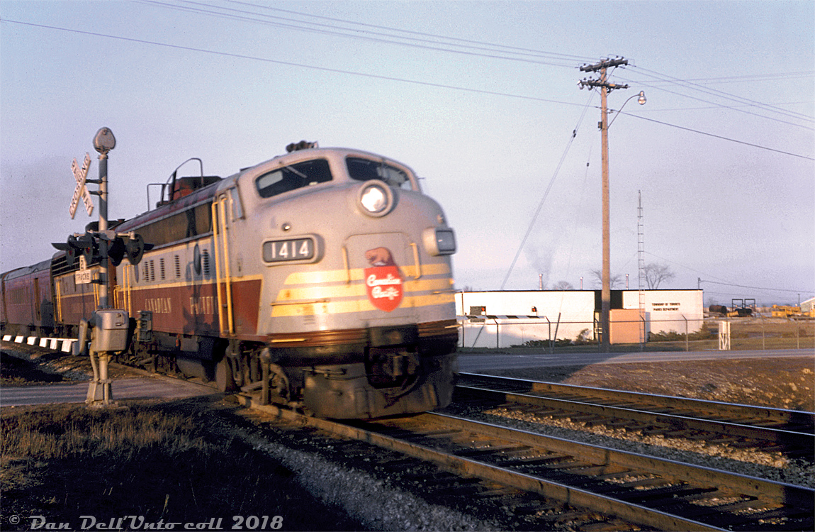 Speeding through what was then known as "Toronto Township" but soon to be renamed Mississauga, CP FP9 1414 and a 1900-series F7B head a westbound passenger train over Mavis Road grade crossing on the Galt Sub, past the Township of Toronto Parks Department building and compound lot on the Erindale/Cooksville border. The train is most likely a Friday evening CP #337 (Toronto-Detroit, via Galt-London-Windsor), running with a conventional consist instead of the usual "Dayliner" Budd RDC cars. If on time, it would be around 7:25pm when this photo was taken, as #337 had departed from Union Station at 7pm and is speeding towards its next (flag)stop at Milton Station for 7:40pm.  This unlabeled slide taken by unknown Toronto-area photographer took a bit of guesswork to figure out: the location was eventually narrowed down to the Galt Sub somewhere in Mississauga, but what train this was remained a mystery. By May 1965 (the slide process date) the only regular conventional trains on the Galt Sub had been cancelled the previous year in April of 1964 (CP #21/22), leaving just the Dayliner (RDC) trains. It was possible the photographer was "tardy" in getting the slide developed on time, but the sun angle meant this was an evening shot and the old 21 was a morning train. After talking with Ray Kennedy of Old Time Trains, it was concluded this was most likely a Friday CP #337 running with a conventional consist instead of the usual Dayliners.  Years later, this grade crossing would be the exact spot the November 10th 1979 Mississauga train derailment occurred, where an eastbound CP freight (lead by three GO Transit F40PH's) derailed due to an overheated plain-bearing journal on one of the cars, scattering tank cars loaded with chemicals across the crossing and causing some of them to rupture, catch fire and explode. Burning propane tank cars, and the risk of a leaking chlorine tank car in the middle of the derailment spreading chlorine gas forced a large-scale emergency response and the evacuation of over 200,000 people and over 80 square kilometers of Mississauga (miraculously, there were no casualties).  Today Mavis Road at this location is now an underpass (it was grade-separated in the years following the incident), and the explosions right after the derailment occurred destroyed half of the Parks Department building in the background (later fully demolished). CP got out of the passenger business decades ago, but GO Transit presently runs a number of weekday Milton-line commuter trains through here with station stops nearby.  Original photographer unknown/not listed, Dan Dell'Unto collection slide.