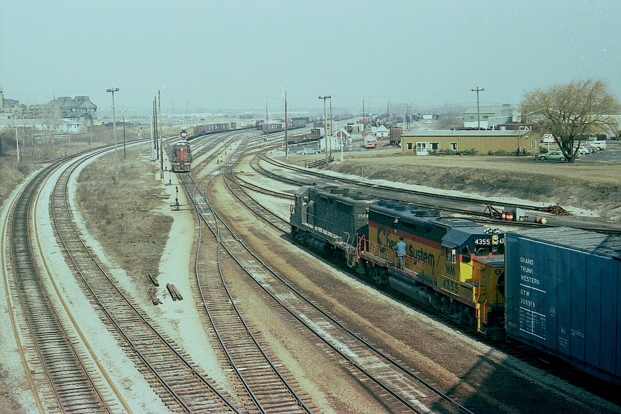 Yeah, it is only March but what a warm and hazy day it was. Nice enough that I drove over to the CN yard before going to work (this is a Friday) to see what was going on. The 6 or 8 CN Geeps based here appeared to be almost all out on assignment, you could say; and I was about to leave when this Chessie transfer came in from the States. It was rare for me to see one at CN in the Falls, and I do not have any idea how often they came over. Maybe in the night, maybe while I was at work, I dunno. Perhaps someone on the group can enlighten us. C&O 3584 and WM 4355 are seen emerging out from under the shadow of the Victoria Av overpass. Check "time machine" to see what is left of this once-bustling CN facility. (Hint: Its gone)