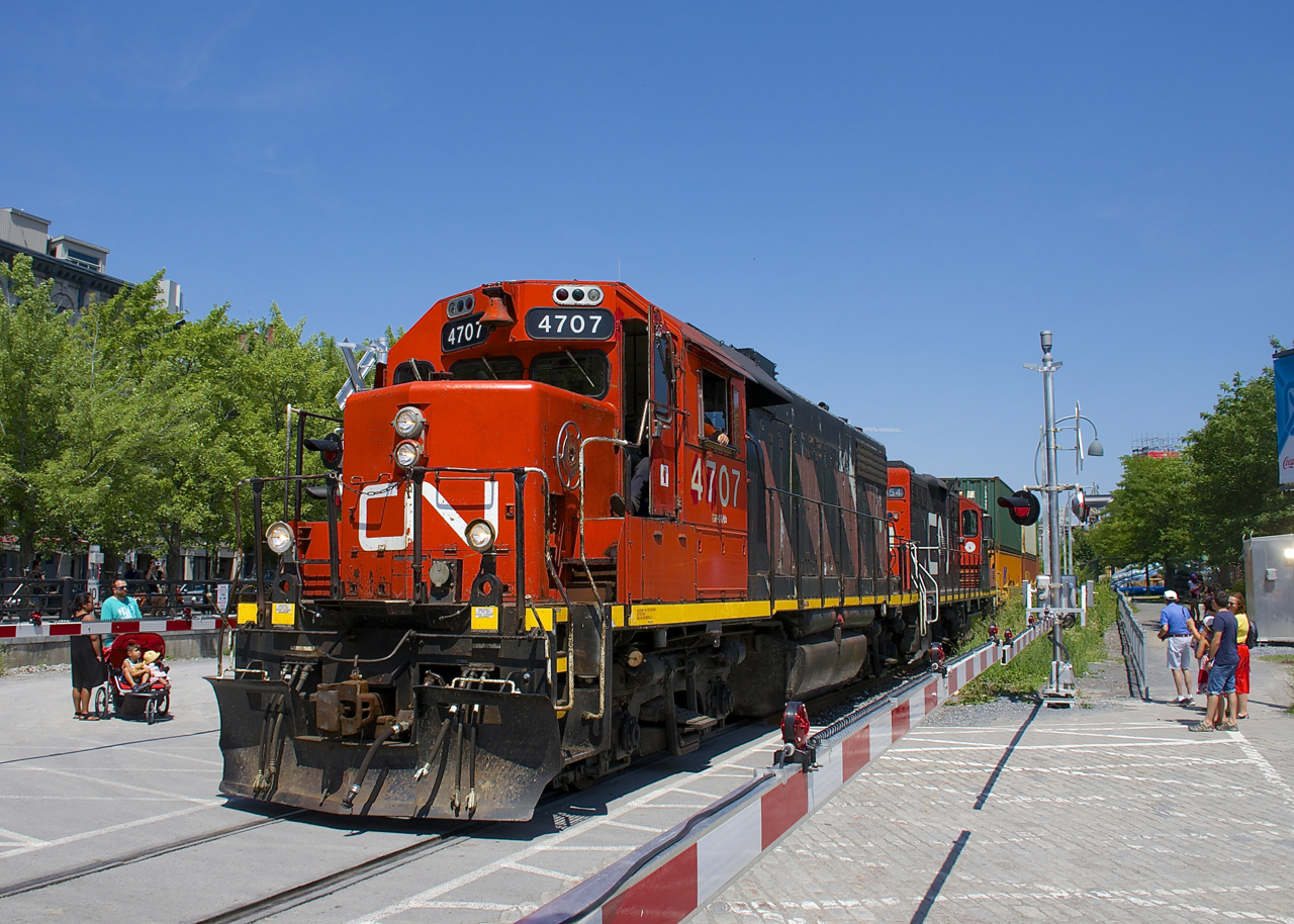 The Pointe St-Charles Switcher is leaving the Port of Montreal with CN 4707 & 7054 & for power and a mostly intermodal train as it passes a crossing, with newly in use gates down.